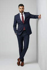Man in navy two-piece slim-fit suit with peak lapels and burgundy tie.
